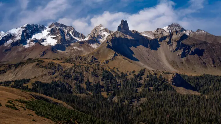 Snowy alpine peaks under a blue sky with a forested valley below.