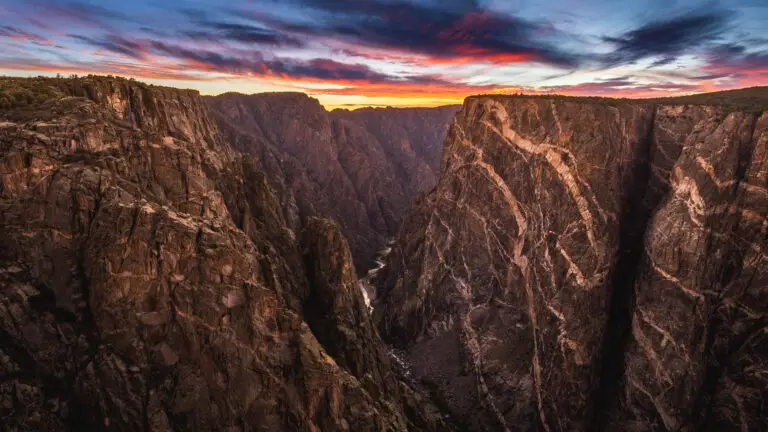 Dramatic sunset over a deep canyon with jagged rock walls and a narrow river at the bottom